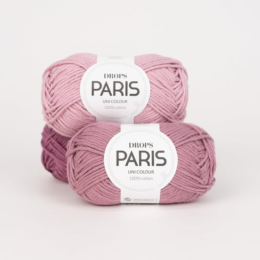 Drei Knäuel der Wolle DROPS Paris in den Farben 60 malve (hinten), 58 puderrosa (oben) und 64 amethyst (vorne).