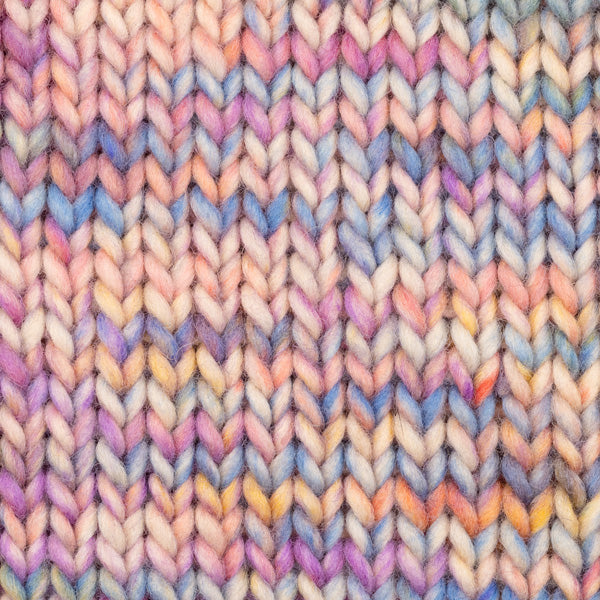 Detailaufnahme eines Strickstücks mit der Wolle DROPS Snow in der Farbe 143 feenmärchen print. Die Farbe besteht aus cremefarbenen, orangen, blauen, rosafarbenen und lila Abschnitten.
