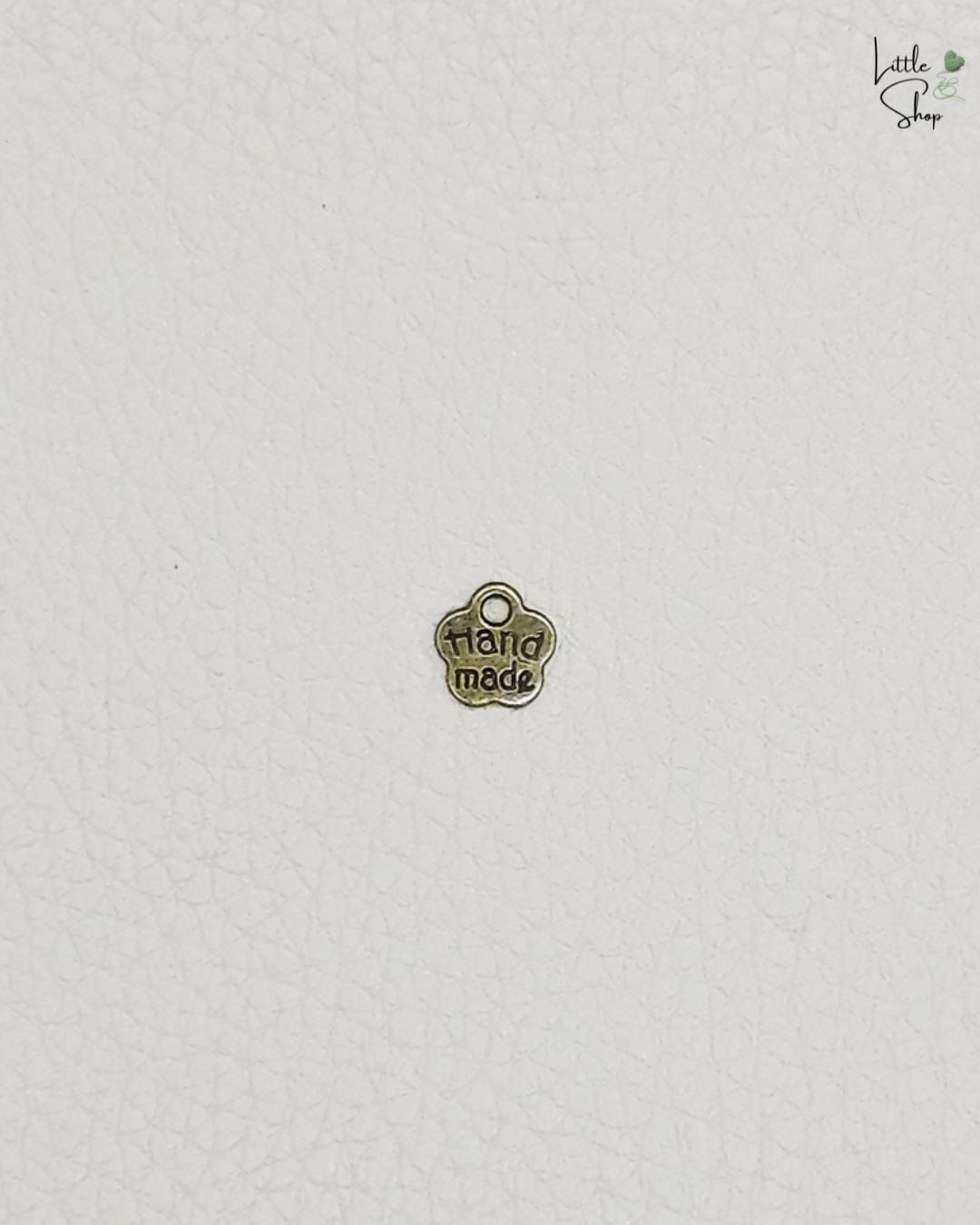 Kleines Metallabel in Blumenform in antikgold mit dem Schriftzug Handmade und einer Ausstanzung, um das Label anzunähen oder aufzuhängen.