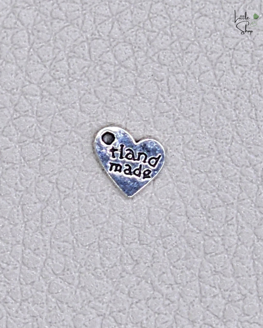Silberfarbenes kleines Metallabel in Herzform mit dem Schriftzug Handmade und einer Ausstanzung, um das Label anzunähen oder aufzuhängen.